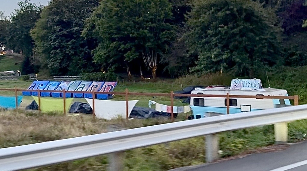 Painted blue 'Art Farm' awnings and banners set up beside the road with a Buy Sell Trade sign and a vintage RV, seen from the road at dusk