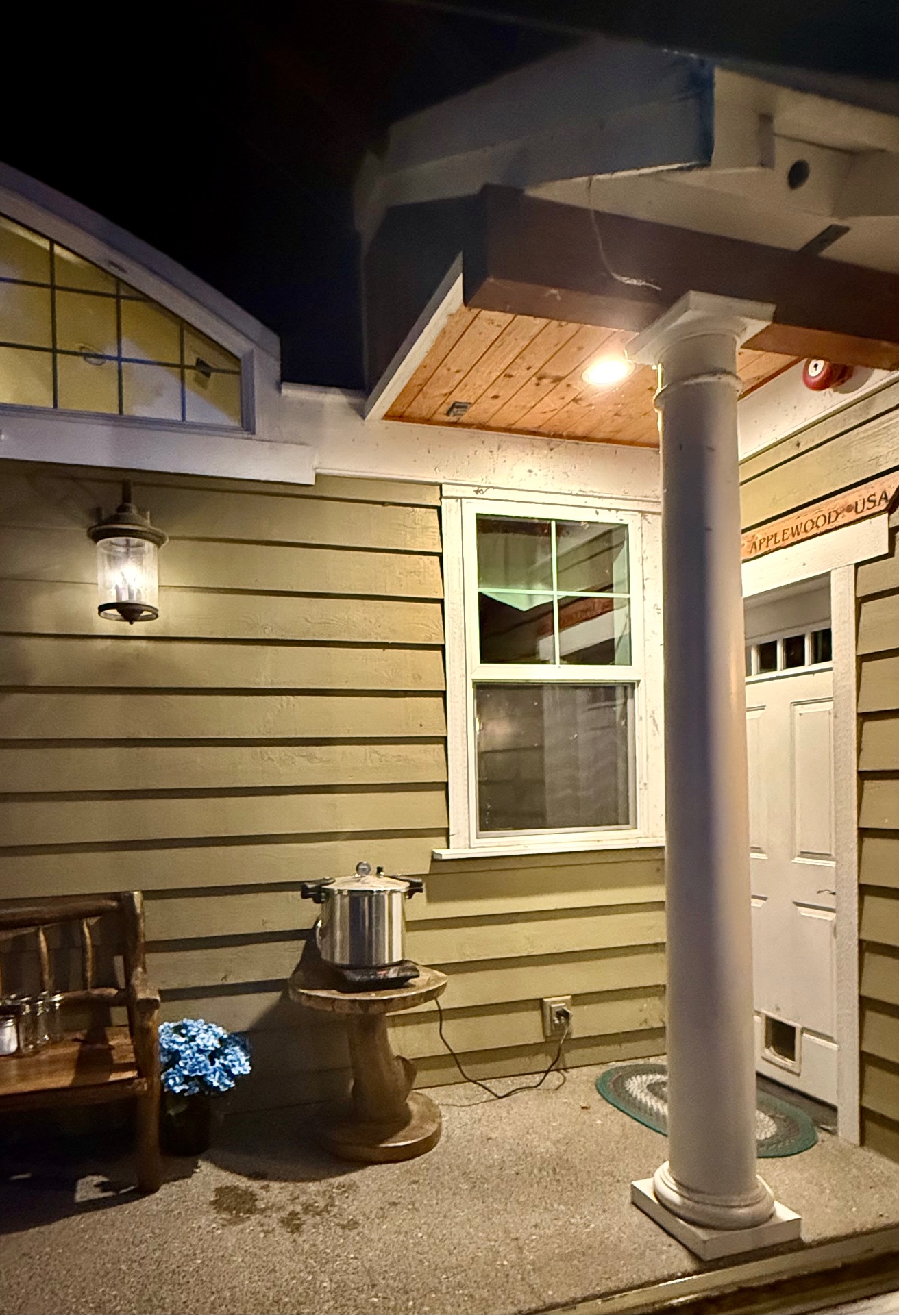 A pressure canner on a wooden stump table on the lit front porch at night