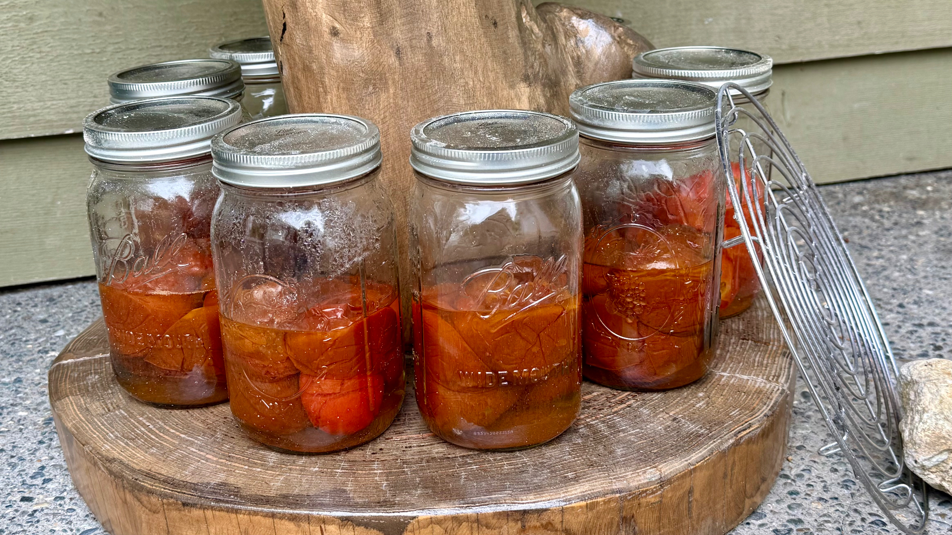 Sealed jars of canned heirloom tomatoes cooling on a round wooden slab