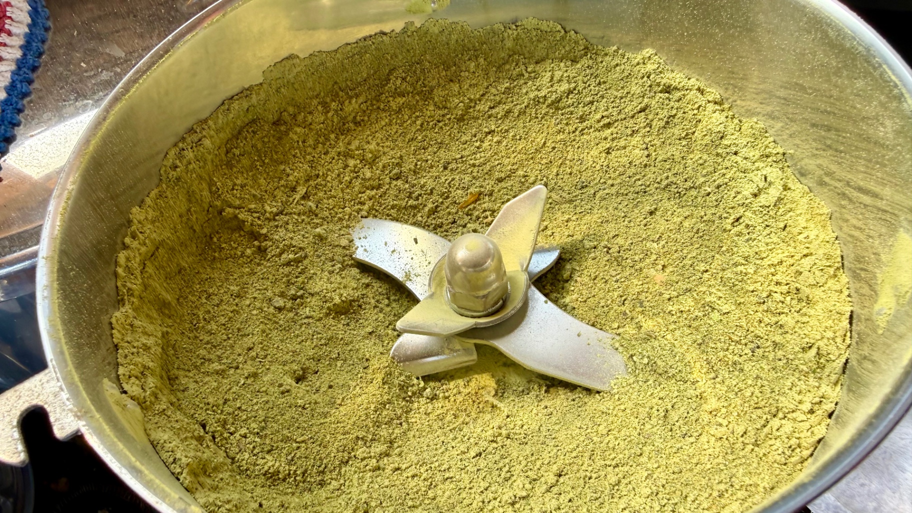 Finely ground greenish-yellow dried prairie grass in a stainless steel grinder bowl