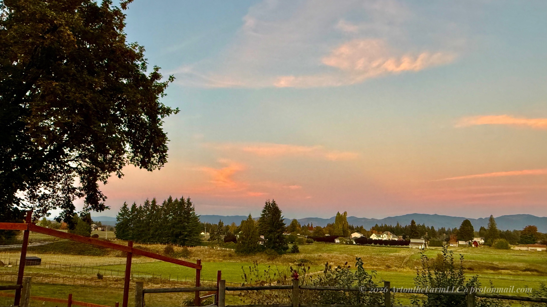 Soft pink sky over the fields and distant hills, framed by a big tree and fence