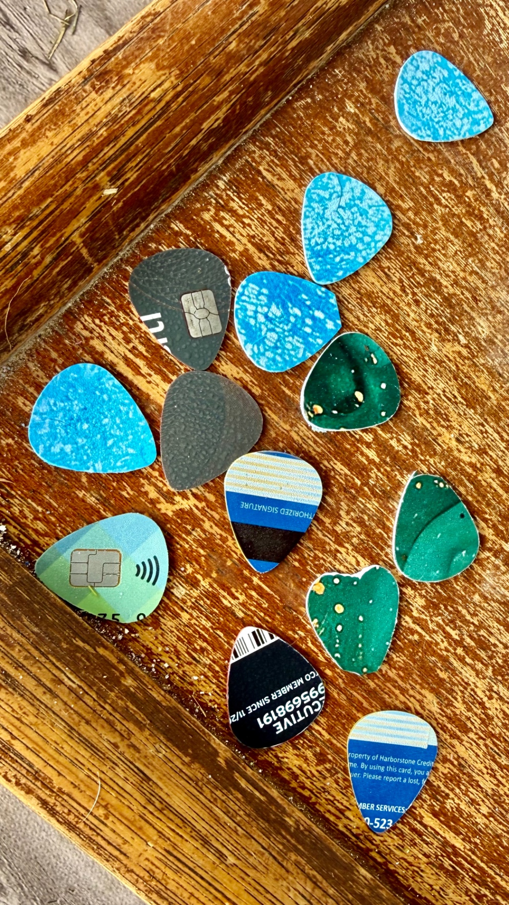Close-up of hand-punched guitar picks in blue, green and grey scattered on a weathered wooden surface