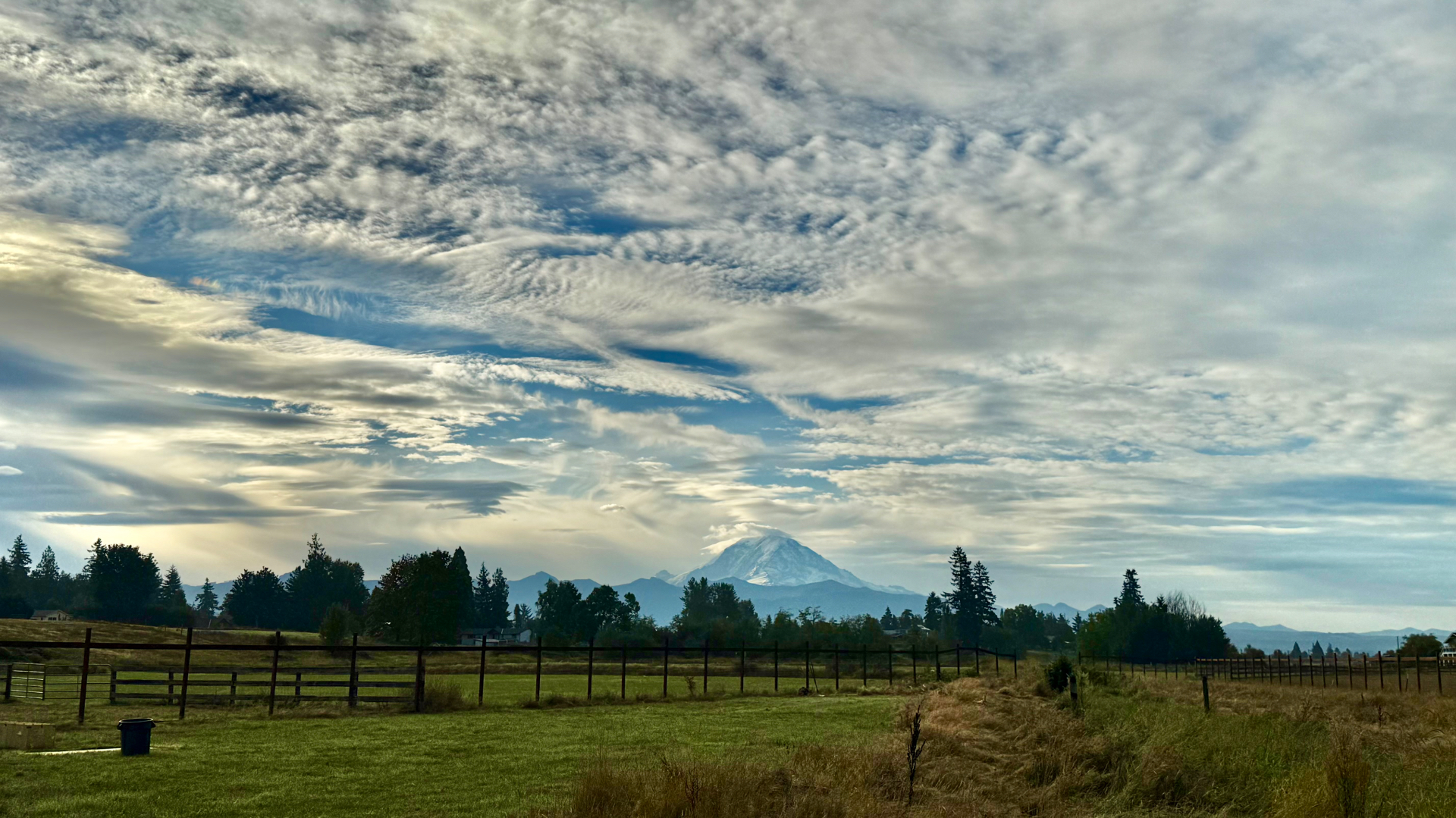 Wide view across the farm field toward Mount Rainier under a textured, cloud-filled fall sky