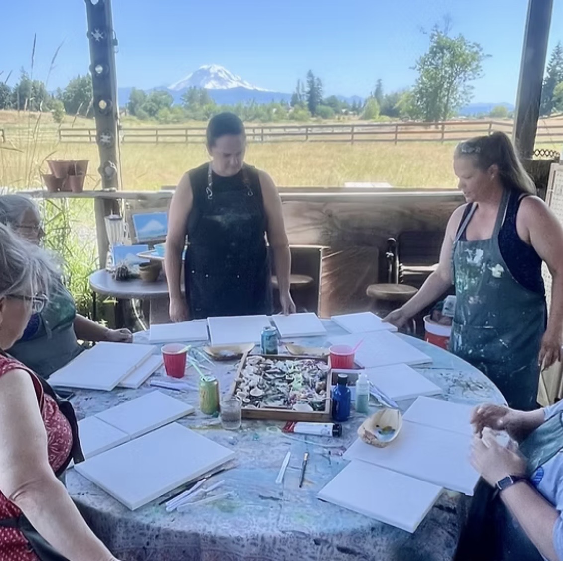 A group painting on blank canvases around a farm table with Mount Rainier behind them