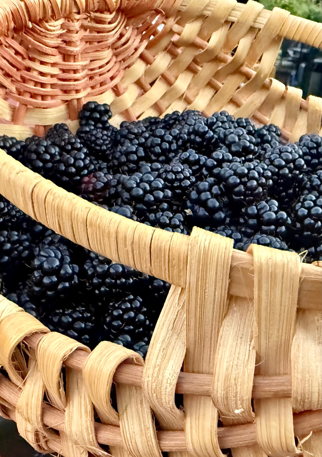 A woven wooden basket overflowing with glossy ripe blackberries, wide wooden handle visible