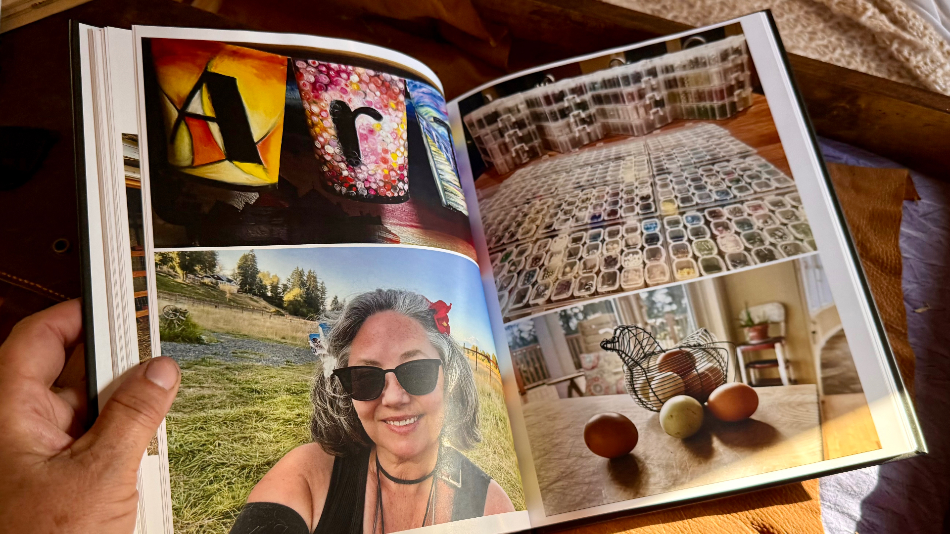An open album spread with glass art letters spelling Art, a colorful bottle, a wall of small sticker containers, a selfie in the pasture, and a wire chicken holding eggs on a wooden table
